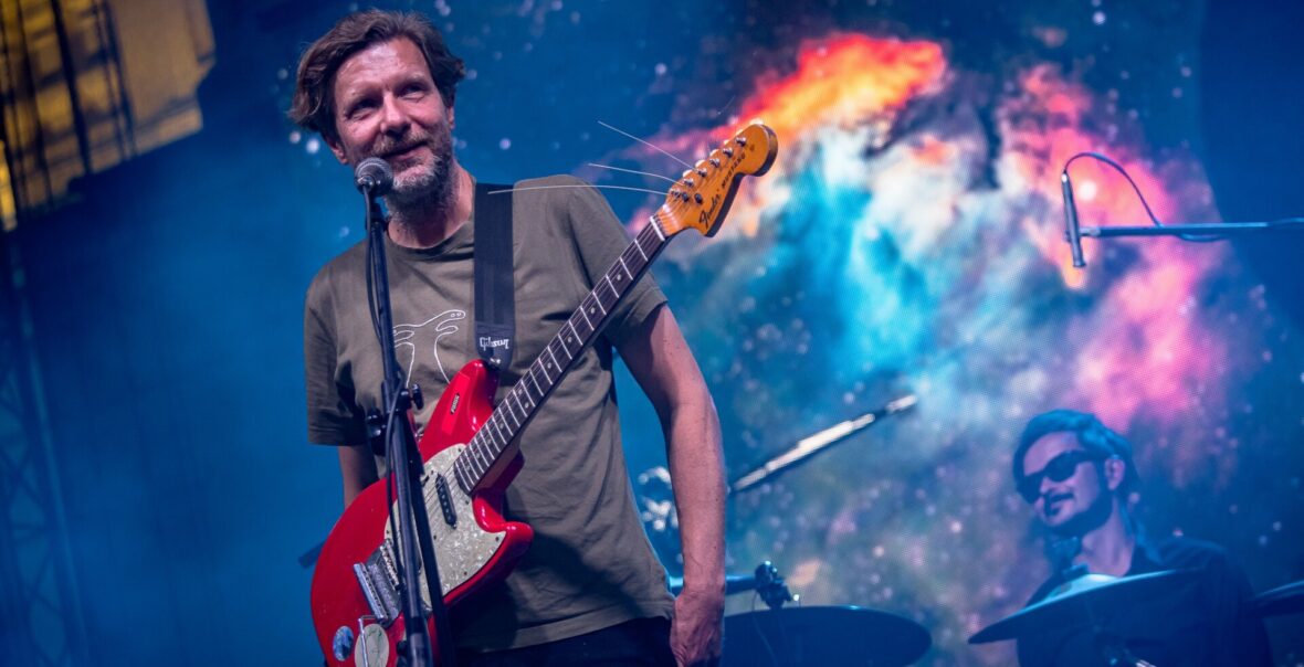 Koncert muzyki współczesnej. Na scenie muzyk z gitarą elektryczną oraz perkusista.